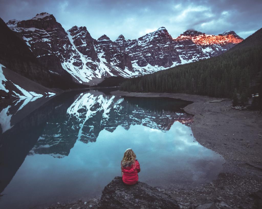 Woman sitting on rock in front calm body of water and mountains view
Photo by Kalen Emsley on Unsplash